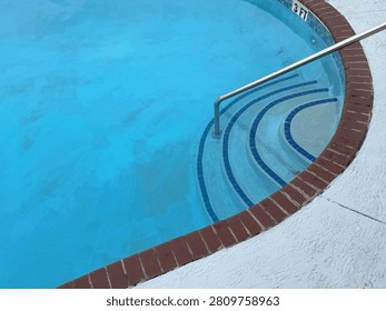 Concentric arc pool steps lined with blue tiles and bisected with a steel hand rail, angled view. Organic shape pool is lined with bricks. Myrtle Beach, SC 2026
