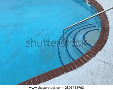 Concentric arc pool steps lined with blue tiles and bisected with a steel hand rail, angled view. Organic shape pool is lined with bricks. Myrtle Beach, SC 2026