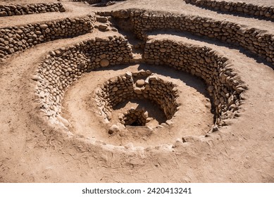concentric wells dug into the rock by the Inca people in the desert with walls of brown stone and sand in the desert in Cantalloc Nazca Peru
