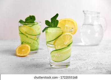 Concept 2 glasses with water and fresh slices of cucumber and lemon with mint on a light concrete background in a high key