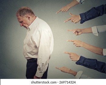 Concept Of Accusation Guilty Businessman Person. Side Profile Upset Old Man Looking Down Many Fingers Pointing At Him Isolated Grey Office Wall Background. Human Face Expression Emotion Feeling 