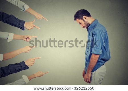 Concept of accusation guilty person man. Side profile sad upset man looking down many fingers pointing at him isolated on grey office wall background. Human face expression emotion feeling