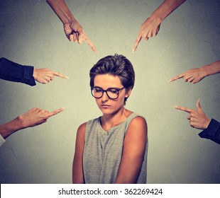 Concept of accusation guilty shy person girl. Sad embarrassed upset woman in glasses looking down many fingers pointing at her isolated grey wall background. Human face expression emotion feeling