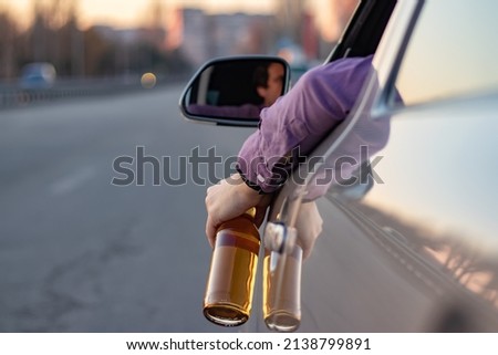 concept of alcohol, dangerous driving. drink and drive. man drinks off a bottle of beer while driving car. driver throws the bottle out of the car window. drunk driving.