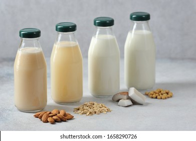 Concept alternative to cow's milk.  Bottles with coconut, oat, soy and almond milk.  Next to the bottles are pieces of coconut, almonds, oatmeal and soybeans.  Light background.  Close-up.