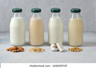 Concept alternative to cow's milk.  Bottles with coconut, oat, soy and almond milk.  Next to the bottles are pieces of coconut, almonds, oatmeal and soybeans.  Light background.  Close-up.