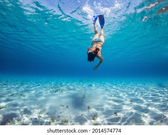 Concept of aquatic physical activity in older people. Sporty lady going underwater with mask and flippers. Stunning transparent and blue water sea. Exploring an impressive clear and clean sea.