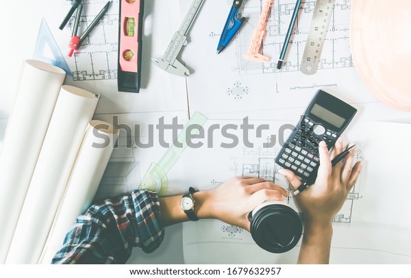 Concept architects, Hand of\
asian young man engineering use calculator for calculation number\
of structural materials writing On the desk with a blueprint in the\
office.