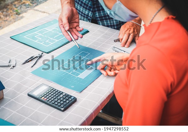 Concept architects, Hand of two Asian young\
women and man engineering use calculator for calculation number of\
structural materials writing On the desk with a blueprint in the\
office. teamwork