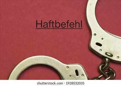 Concept For Arrest, Handcuffs Next To The German Word Haftbefehl, Translation Arrest Warrant On A Red Paper Background, Germany