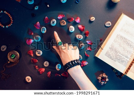 Concept of astrology and horoscope. A woman's hand points to the stones with the signs of the zodiac, laid out in a circle and decorated with rose petals. Divination and magic.