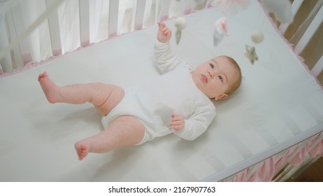 Concept Of Baby And Childhood Beautiful Baby Girl Laying Down In Her Baby Cot And Looking Up At The Cot Toys Playing And Moving With Her Cute Legs