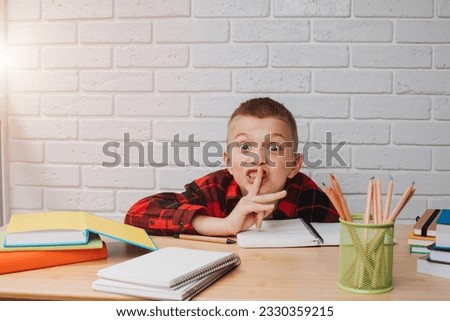 Concept back to the school. A boy in the process of studying sits at a table with unigami, notebooks and pencils. Front view