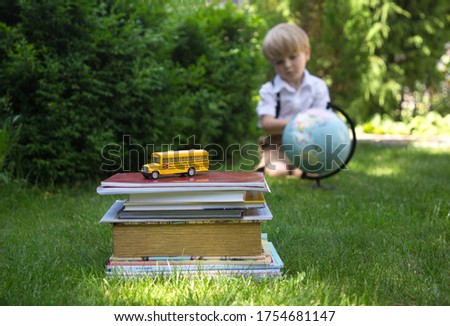 concept back to school. A stack of books and notebooks with a toy school bus. in the background in defocus little student with a globe. Summer is over, school is starting. Knowledge is power. 