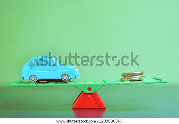 Concept of a balance between a car and\
money on green background. Close up, selective\
focus