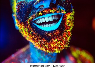 Concept. A bearded man smiles. Portrait of a bearded man painted in fluorescent powder.