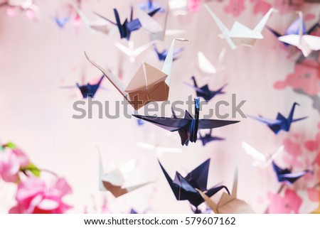 The concept of the beautiful scenery on holiday - the traditional Japanese origami on strings in the background graphics and pink of sakura blossoms. Many swans made out of paper. Soft focus.