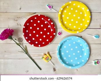 The concept of Birthday party accessories. Closeup a set of colorful polka dots paper plates , mini birthday candles and a pink carnation flower on wooden background. Selective focus .