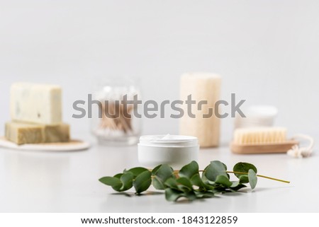 Concept of bodycare and skincare cosmetics. Selective focus on moisturizing and pampering face cream near green eucalyptus plant against white copy space background in bathroom