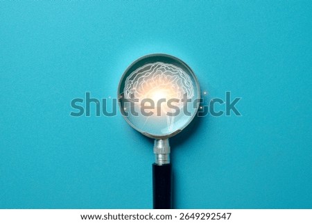 Concept of brainpower and creative thinking. A magnifying glass focuses on a glowing brain icon on light blue background idea for intelligence, innovation,psychology,mental clarity, self-awareness.