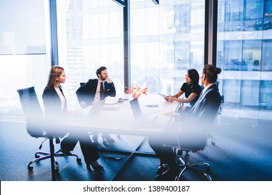 Concept of brainstorming and briefing, positive diverse male and female financial experts discussing information during working time in conference room sitting at desktop with laptop devices