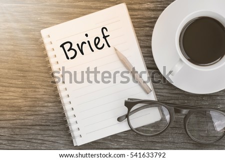 Concept Brief on notebook with glasses, pencil and coffee cup on wooden table.