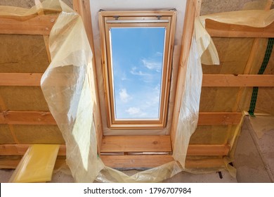 Concept of building improvements. Low angle view of house under construction, mansard with environmentally friendly and energy efficient skylight window against blue sky and wooden roof truss planks