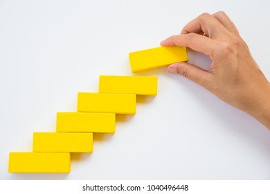 Concept Of Building Success Foundation. Women Hand Put Red Wooden Block On Yellow Wooden Blocks In The Shape Of A Staircase