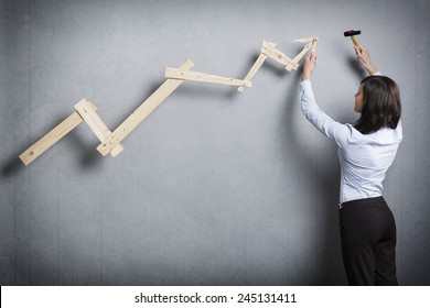 Concept: Building Your Own Successful Career Or Business. Confident Businesswoman With Hammer In Hand Building  Business Graph With Positive Trend, Isolated On Grey Background.