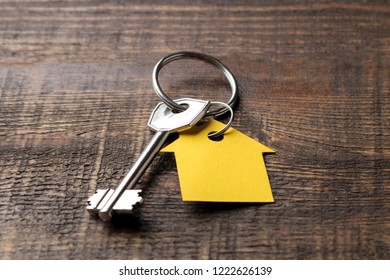 The concept of buying a home. Keys with keychain house on a brown wooden background close-up.