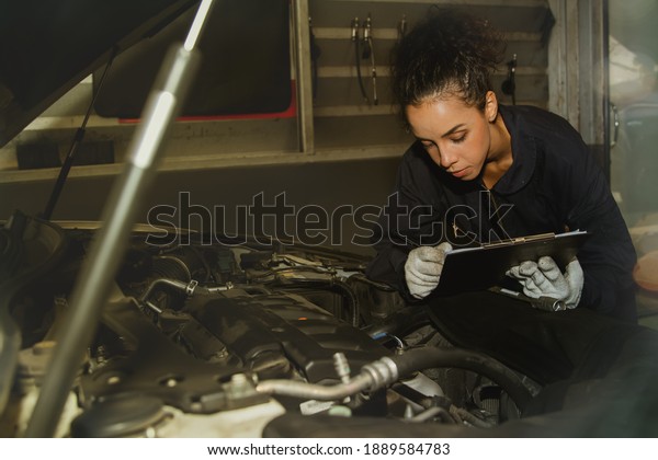 Concept of car maintenance in service stations\
: Female mechanic holds a clipboard to inspect the customer\'s\
vehicle and checks the engine system for maintenance purposes for\
safety before\
traveling.