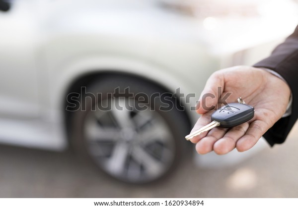 Concept car rental, car salesman\
A man in a suit\
with a car key in his\
hand
