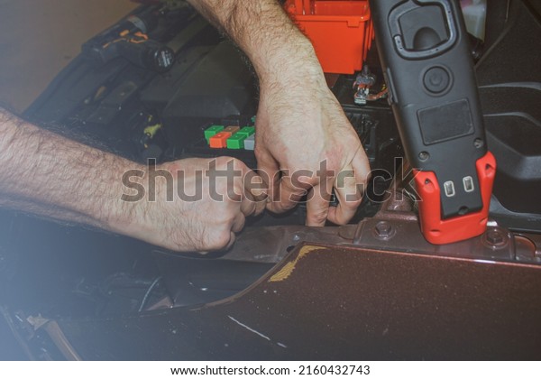 The concept of car service, repair, tuning,\
maintenance. The car electrician fixes problems in the electronics\
of the car. Hands of an electrician working with an electrical unit\
in a car close-up.