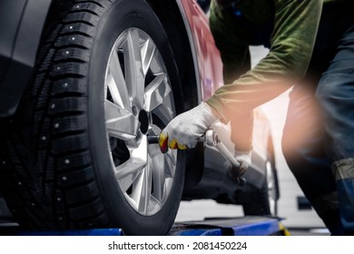 Concept car service replacement of winter and summer tires. Mechanic unscrews wheel bolts from red auto.