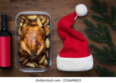 Concept Of Celebrating Christmas And New Year At The Dinner Table. Christmas Chicken, Wine And Santa Hat On Wooden Background, Top View