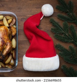 Concept Of Celebrating Christmas And New Year At The Dinner Table. Christmas Chicken, Wine And Santa Hat On Wooden Background, Top View