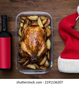 Concept Of Celebrating Christmas And New Year At The Dinner Table. Christmas Chicken, Wine And Santa Hat On Wooden Background, Top View