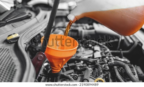 Concept changing motor oil in car\
engine at garage service station. Closeup move yellow\
lubricant.