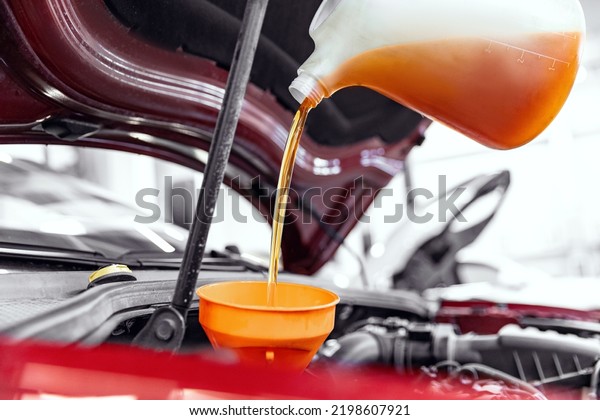 Concept changing motor oil in car\
engine at garage service station. Closeup move yellow\
lubricant.