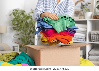 The concept of charity and clothing recycling. A woman puts colorful bright different clothes in a box. - Powered by Shutterstock