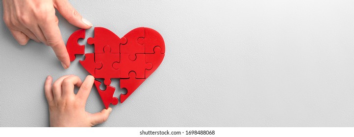 The concept of charity, love, donate and helping hand. International cardiology day. A woman and child arranges red heart shape puzzles. Symbol of helping others.