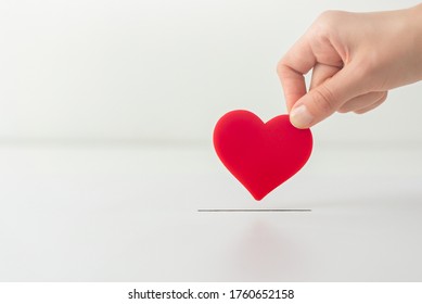 The Concept Of Charity, Love, Donate And Helping Hand. Woman’s Hand Places Heart In The Donation Slot. Donor Of Blood Or Human Organs, Saving Lives.