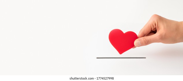 The Concept Of Charity, Love, Donate And Helping Hand. Woman’s Hand Places Heart In The Donation Slot. Donor Of Blood Or Human Organs, Saving Lives.