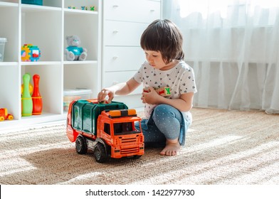 The Concept Of Childhood And People Is A Happy Three Year Old Girl Playing With A Toy Car At Home. Girl Playing Games For Boys. The Child Is 3 Years