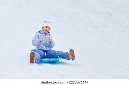 Concept of childhood, sledding in winter. Happy little girl is rolling down the hill on a sled.