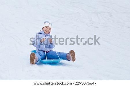 Concept of childhood, sledding in winter. Happy little girl is rolling down the hill on a sled.