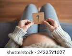 Concept of choosing baby name, Pregnant woman holding paper with question mark.