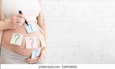 Concept of choosing baby name. Pregnant woman with question marks on paper stickers on tummy, panorama with empty space
