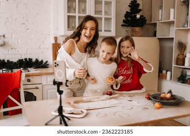 The concept of Christmas. Mom and two children cook festive food together on Christmas day and communicate with relatives online using the phone and technology in the kitchen at home. Selective focus - Powered by Shutterstock