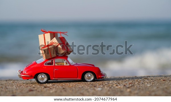 Concept of Christmas and New Years vacation at\
sea, ocean.Christmas holidays in warm countries.Travel at sea by\
car.Greeting card.Close-up red car with gifts on seashore on\
sand.Lebedevka\
09.11.2021